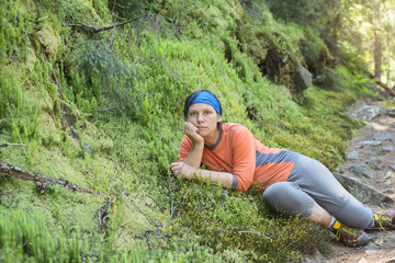 Naklejka na ściany i meble Hiker woman relaxing, lying on the green moss, looking at camera