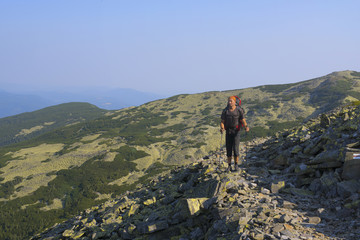 Hiker with backpack goes on rocky path in the mountains.