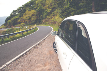 A white car is parked in the side of the road in the summer on a asphalt road. Image has a vintage effect.
