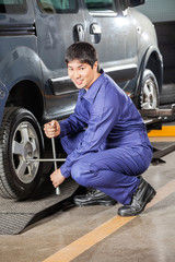 Fototapeta na wymiar Confident Mechanic Fixing Car Tire With Rim Wrench