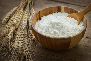 Flour in bowl and wheat on wooden table