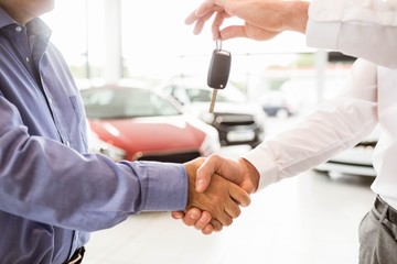 Businessman giving car key while shaking a customer hand