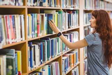 Mature student picking book in library wearing smart watch