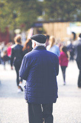 An elderly man is standing in the city. Some unidentified person are walking in the streets. Image has a vintage effect applied.