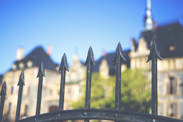 A metal fence with sharp arrows is guarding the beautiful castle. The castle is blurry in the background. Image has a vintage effect applied.