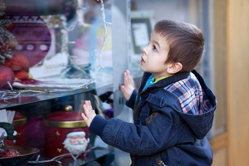 Sweet little boy, looking through a window in shop, decorated fo