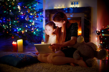 Mother and daughter using a tablet by a fireplace on Christmas
