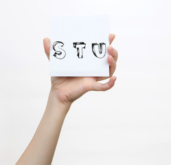 Hand holding a piece of paper with sketchy capital letters S T U, isolated on white.