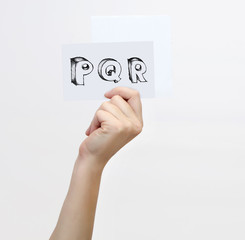 Hand holding a piece of paper with sketchy capital letters  P Q R, isolated on white.