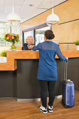 Young woman checking in at a hotel - obrazy, fototapety, plakaty
