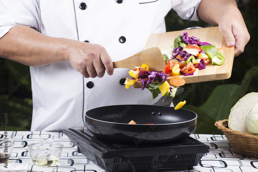 Wall mural chef putting vegetable to the pan