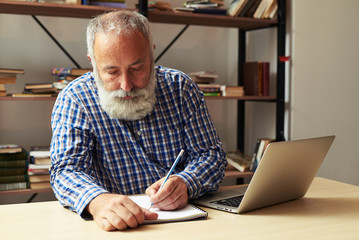 senior man writing in notepad at his working place - Powered by Adobe
