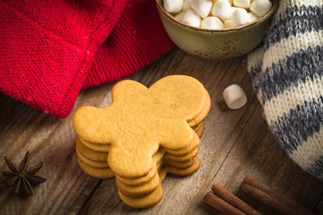 Group of homemade gingerbread man cookies, surrounded with spices, marshmallows and colorful winter sweaters on wooden background, close up