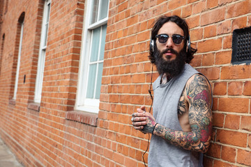 Young tattooed man portrait listening to music against brick wall in Shoreditch, London.