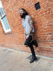 Fototapeta na wymiar Young tattooed man portrait listening to music against brick wall in Shoreditch, London.