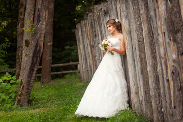 Bride near wooden rustic fence in park