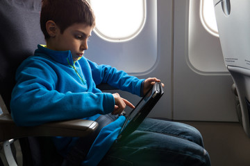 Young kid relaxing using tablet inside airplane.
