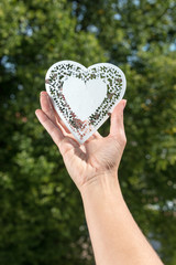 Obraz premium Hand holds up heart made of white metal in a park in front of tr