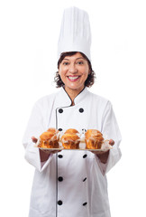 portrait of a mature woman wearing like a chef holding a tray of cupcakes on a white background