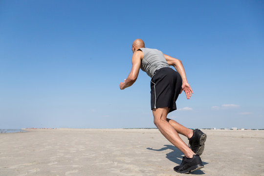 African-american man running on a beach with blue sky