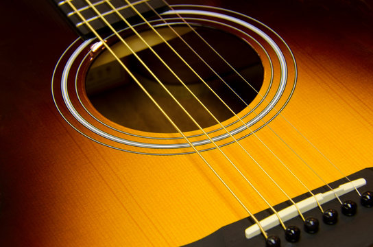 Acoustic guitar closeup with a sunburst finish showing sound hole, rosette, strings, frets, neck, bridge and bridgepins.