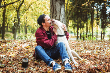 Fototapeta premium man drinking coffee in park and playing with labrador dog