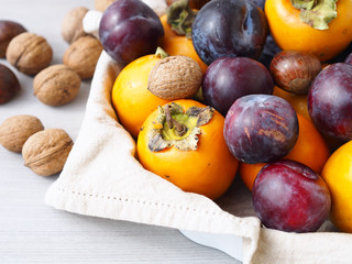Persimmons with purple plums, chestnuts and walnuts. Fall still life