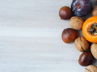 Wooden background with a persimmon, plums, chestnuts and walnuts. Fall still life