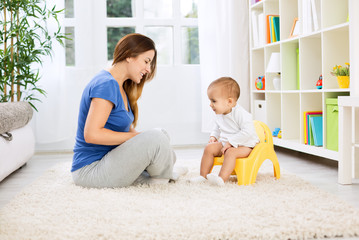 Beautiful mother learning little child how to sitting on potty - obrazy, fototapety, plakaty