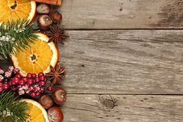 Christmas side border with branches, nuts and orange slices on a rustic wood background