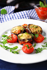 Dish of eggplant with cherry tomatoes and cheese in white plate on wooden table, closeup