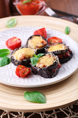 Dish of eggplant with cherry tomatoes and cheese in white plate on wooden table, closeup