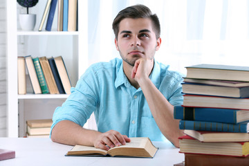 Young man reading book at table in room