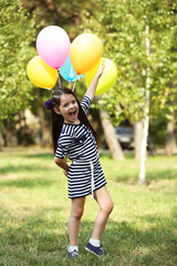 Happy little girl in striped dress with colourful balloons in the park