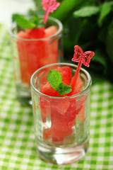Cold watermelon pieces in glasses, on wooden table background