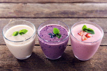 Tasty blueberry, strawberry and milk yogurts in a row on wooden background