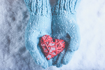 Woman hands in light teal knitted mittens are holding beautiful a entwined vintage red heart on snow. Love, St. Valentine concept