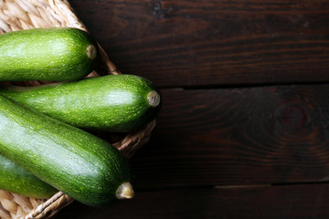 Fresh zucchini in wicker basket on wooden background