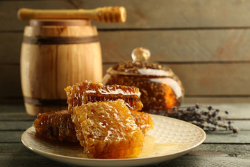 Honeycombs on plate, pot with honey and wooden barrel on wooden background