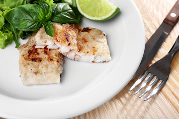 Dish of fish fillet with greens and lime on table close up