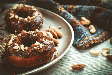 Delicious doughnuts with chocolate icing and nuts on table close up