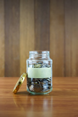 Image of coins in clear bottle with blank label against blurred wooden background. Saving concept.