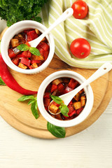 Tasty vegetarian ratatouille made of eggplants, squash, tomatoes in bowls on wooden table background