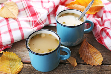 Two mugs of soup and napkin on wooden background