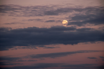 Milky moon in cloudy sky at sunset