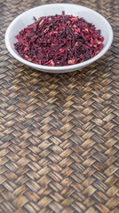 Obraz na płótnie Canvas Dried red hibiscus tea leaves in white bowl over wicker background