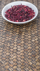 Dried red hibiscus tea leaves in white bowl over wicker background