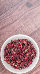 Obraz na płótnie Canvas Dried red hibiscus tea leaves in white bowl over wooden background
