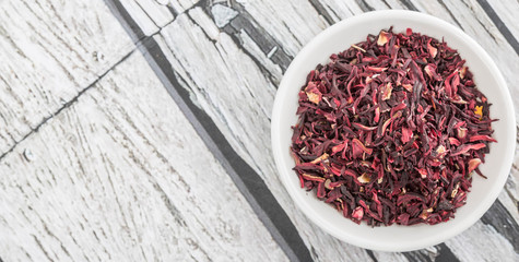 Dried red hibiscus tea leaves in white bowl over wooden background