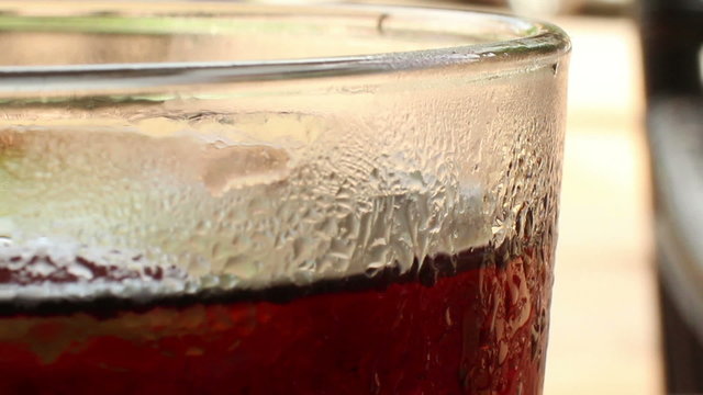 ECU of the top of a glass of cola-colored fizzy drink with indistinct backgro
